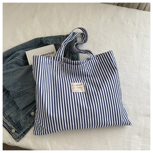 Flat lay of blue striped canvas tote bag with woven label and casual accessories
