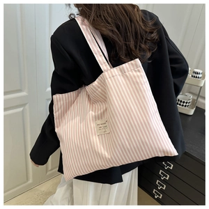 Detail of pink and white striped canvas tote bag worn by a model in casual office style
