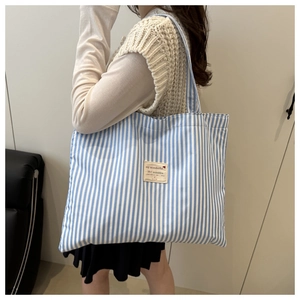 Blue and white striped canvas tote bag detail worn by a model in a casual indoor setting