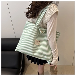 Side view of a large green and white striped canvas tote bag worn on shoulder