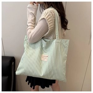 Detail of green striped canvas tote bag with shoulder strap and white textile label