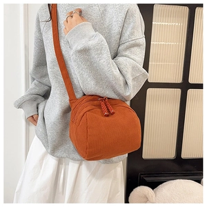 Detail of orange corduroy crossbody bag with dual zippers worn over grey hoodie