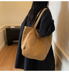 Detail of tan canvas tote bag with black Fashion patch shown on model's shoulder
