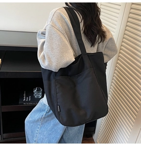 Close-up of black canvas tote bag featuring front pocket and woven fashion label