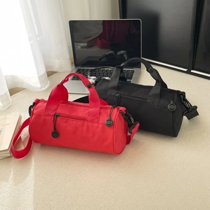 Minimalist cylindrical travel duffel bag in red and black with cross-body strap