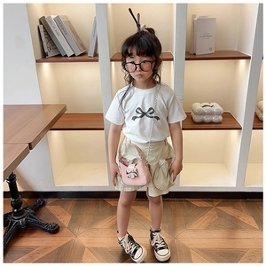 Bambina con borsa a tracolla rosa con fiocco, t-shirt bianca e pantaloncini cargo kaki