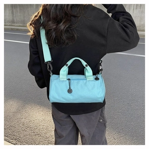 Street style shot of a light blue canvas barrel bag with adjustable strap and handles