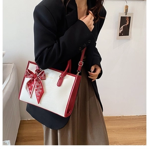 Dettaglio borsa bicolore con motivo a serpente e foulard decorativo a cuori sul manico