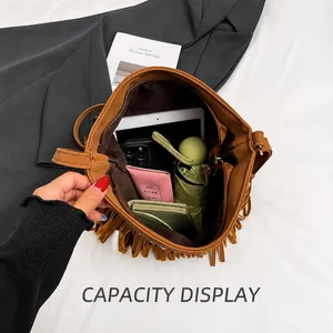 Détail d'un grand sac seau à franges marron contenant une tablette, un téléphone et du maquillage