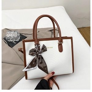 Dettaglio della borsa a mano bicolore con trama serpente e foulard di seta decorativo