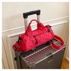 Detail view of red cylindrical travel bag on silver suitcase with detachable strap
