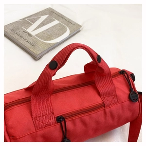 Close-up of red cylinder sports bag with dual zippers and reinforced black handle buttons