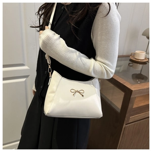 Detail of white faux leather crossbody bag featuring a golden metal butterfly ornament
