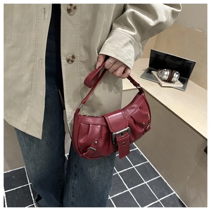 Detail of dark red ruched handbag with silver buckle handle shown in a street style view