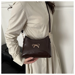 Detail of a dark brown glossy leather shoulder bag with gold butterfly hardware