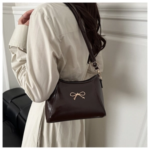 Model wearing dark brown patent leather shoulder bag with gold butterfly bow buckle detail