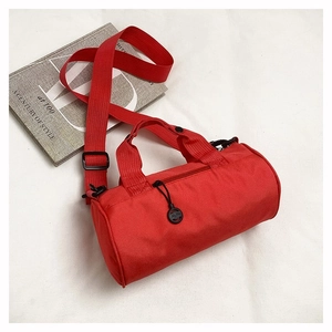 Flat lay of red cylindrical sports bag with adjustable strap beside a fashion book