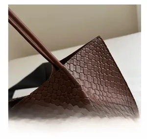 Close-up of deep brown woven leather texture and sturdy strap stitching on the tote bag