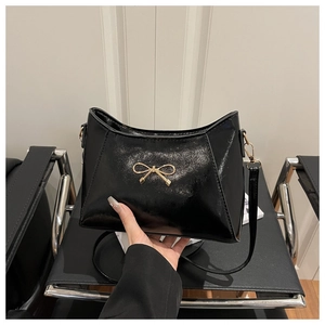 Close-up of glossy black faux leather shoulder bag featuring a gold butterfly buckle detail