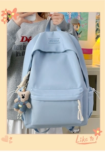 Close-up of light blue nylon backpack featuring a plush bear charm and rope zippers