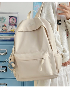 Detail of a beige high-capacity nylon backpack with bear keychain worn by a model