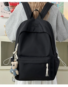 Detail of minimalist black nylon backpack with side drawstring pockets and cute bear charm