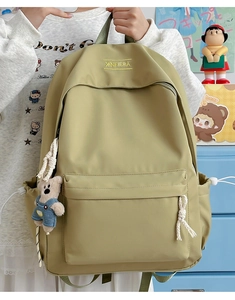 Close-up of light olive green nylon backpack featuring a cute bear plush and embroidery