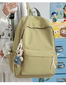 Detail of a light olive green nylon backpack featuring a cute blue bear plush pendant