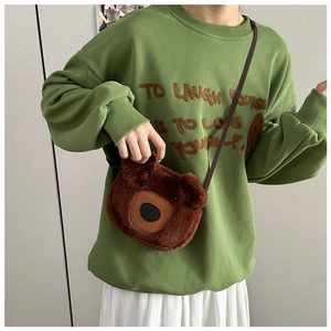 Détail d'un sac bandoulière en peluche ours marron porté sur un sweat-shirt vert