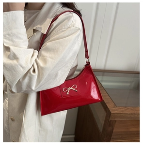 Détail du sac porté épaule en cuir verni rouge avec une boucle nœud dorée élégante