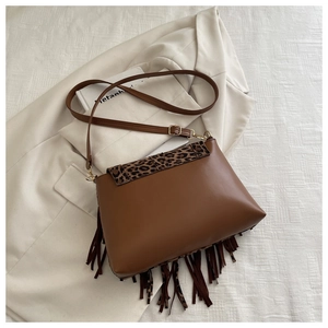 Détail du sac en cuir à franges marron avec rabat léopard posé sur un blazer beige