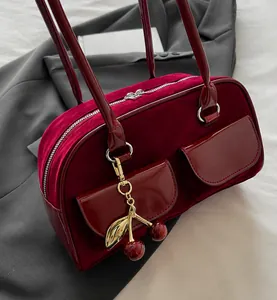 Detail of red suede bag with metal zippers and a decorative cherry leaf charm