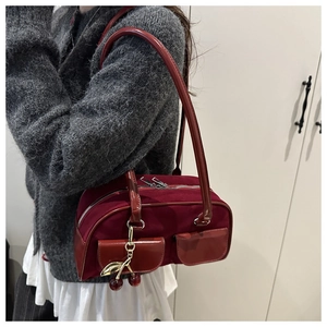 Detail of burgundy suede shoulder bag with dual front pockets and cherry charm