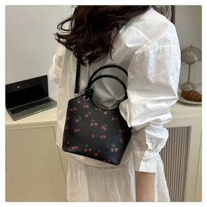Detail of a black cherry print tote bag shown crossbody by a model in a modern home