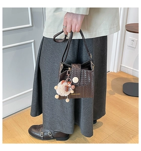 Detail of dark brown woven bucket bag with a plush lion charm and fashion logo