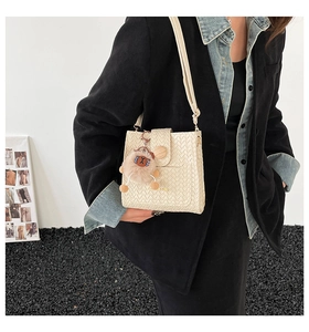 Modell mit schicker cremefarbener Web-Eimertasche, Plüsch-Anhänger und Umhängeriemen