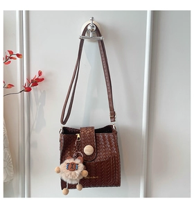 Detail of dark brown woven shoulder bag with golden text and cute plush bear charm