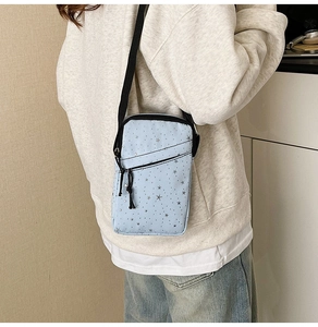 Detail of light blue crossbody phone bag with star patterns on a casual model outfit