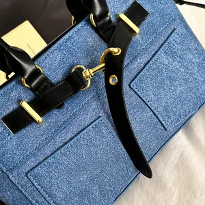Detail of blue denim fabric, black leather handles and shiny gold hardware on the handbag