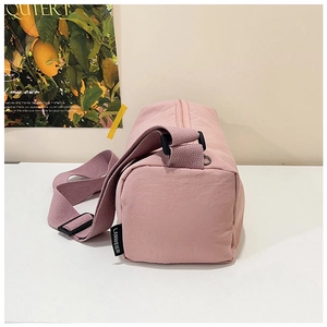 Pink nylon cylindrical crossbody bag featuring top zipper and branded side woven label detail