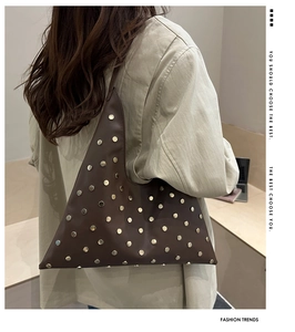 Détail du sac bandoulière triangle en cuir marron avec rivets dorés sur costume