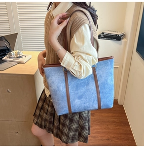 Elegante borsa tote azzurra con manici marroni su una scrivania con laptop e libri