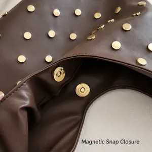 Détail des clous dorés et du fermoir magnétique sur un sac en cuir marron foncé