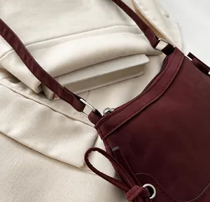 Close-up of silver metal buckle connecting a wine red suede strap to a shoulder bag