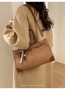 Brown woven tote bag with leather straps and decorative bead charm worn by a model