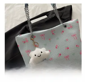 Detail of floral tote bag with plush cloud charm and silver chain strap on white fabric