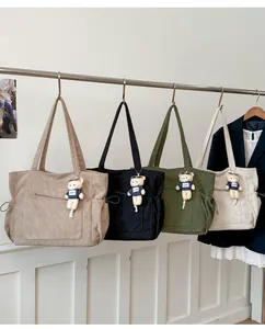 Corduroy tote bags in four colors with teddy bear charms hanging on a metal rack