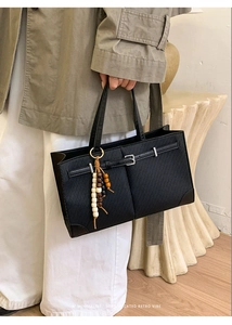 Macro detail of black retro tote bag with textured finish and decorative wood bead charm