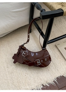 Detail van donkerbruine lakleren hobo-tas met zilveren ogen en een beren-bedeltje