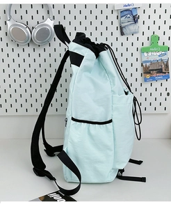 Detail view of the mint green drawstring backpack with side pockets on a white wall